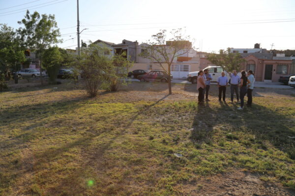 Eine Gruppe von Menschen steht auf einer Wise nahe eines Wohngebiets in Saltillo, Mexiko. Es ist Nachmittag, die Sonne steht tief.