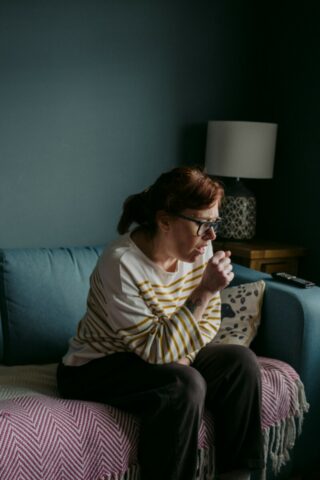 A women in a white and red striped jumper is sitting on a green sofa coughing.